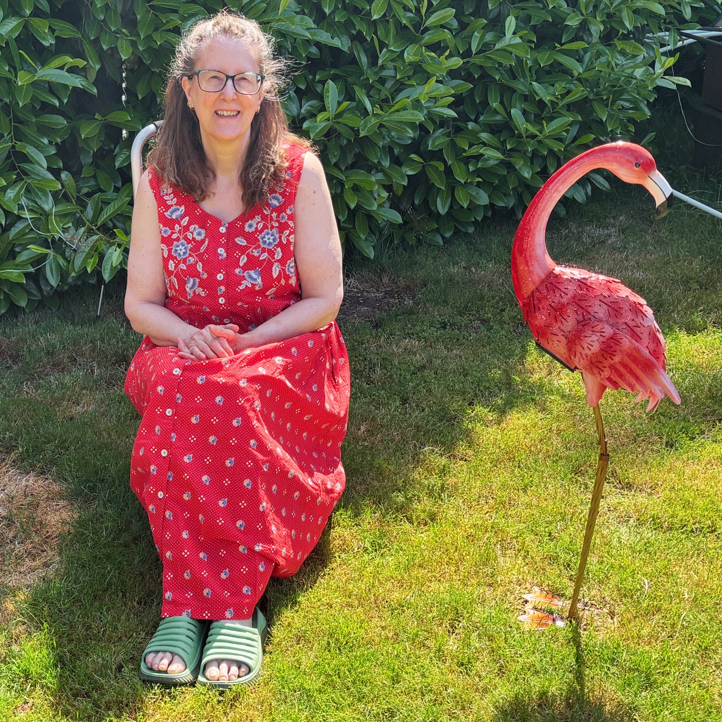 Barbara in a red dress sitting on grass next to a pink flamingo statue.