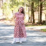 Melissa in a red floral dress standing on a paved road with trees in the background