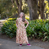 Melissa in a floral dress standing in a park with greenery and trees in the background