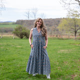 Melissa in a long blue dress standing in a grassy field with trees and hills in the background