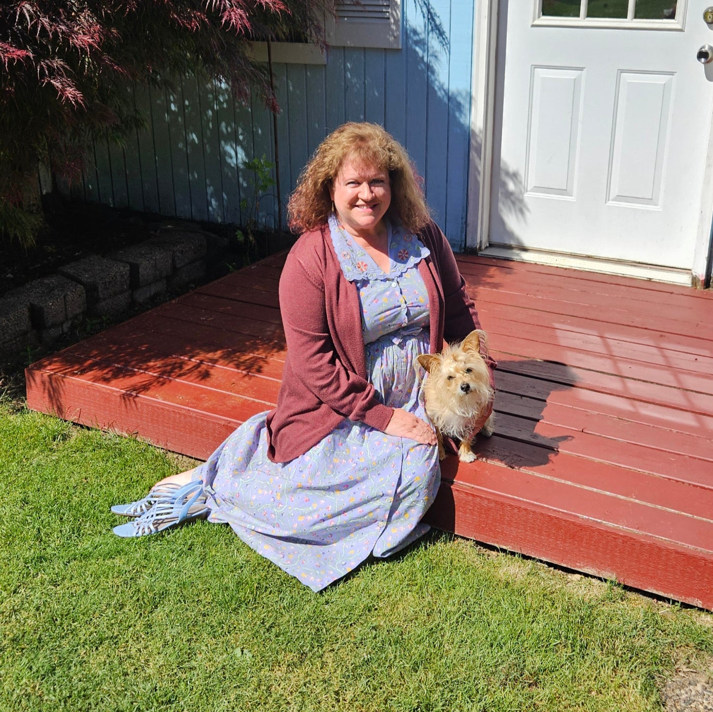 Debra sitting outside with little dog wearing beautiful blue dress long and red cardigan