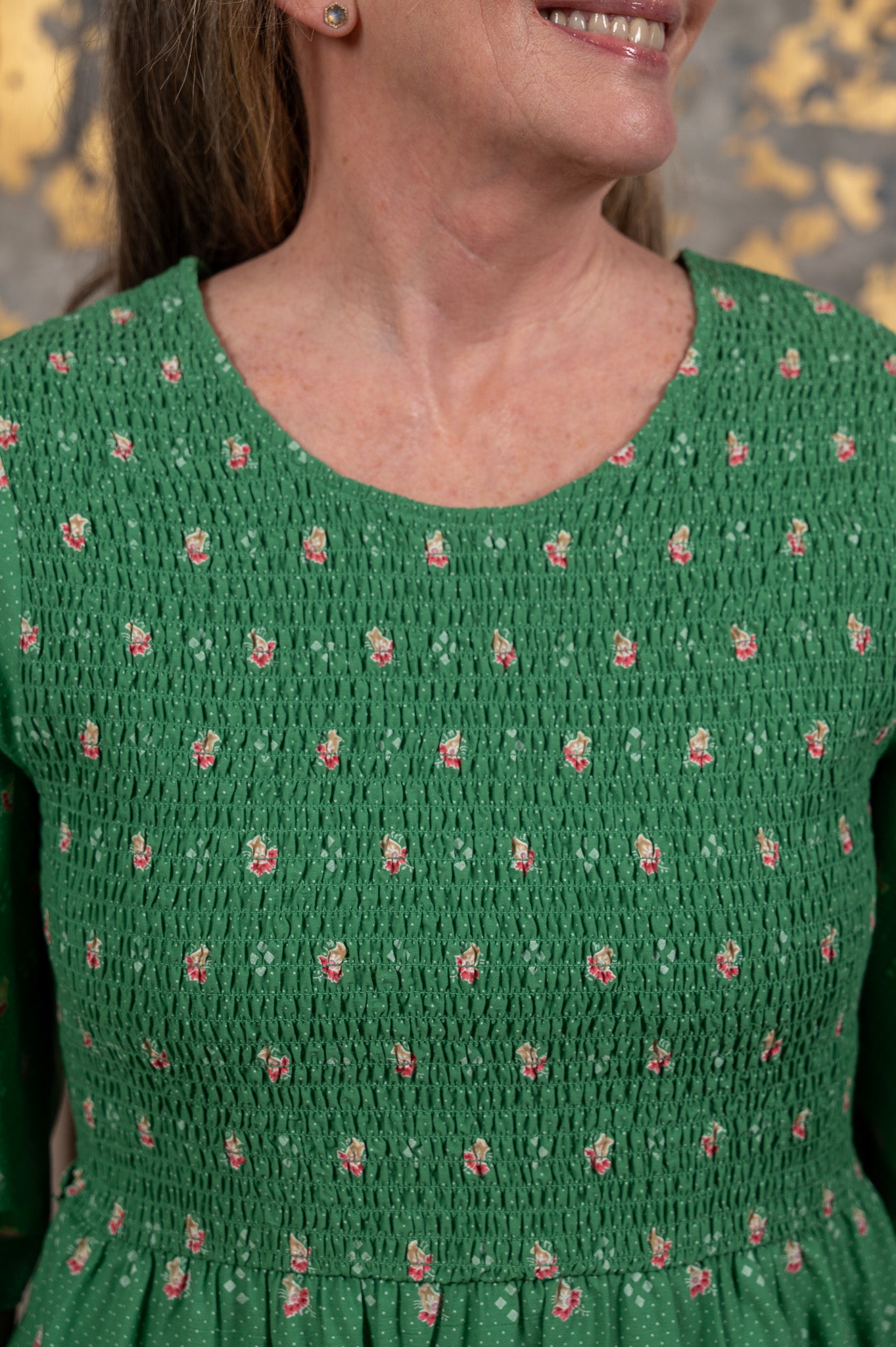 Woman wearing a green dress with floral pattern against a gold leaf background