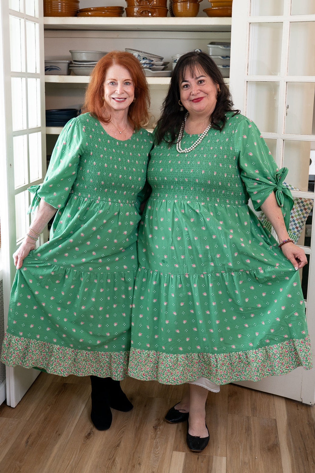 Two women in matching green dresses standing in a kitchen.