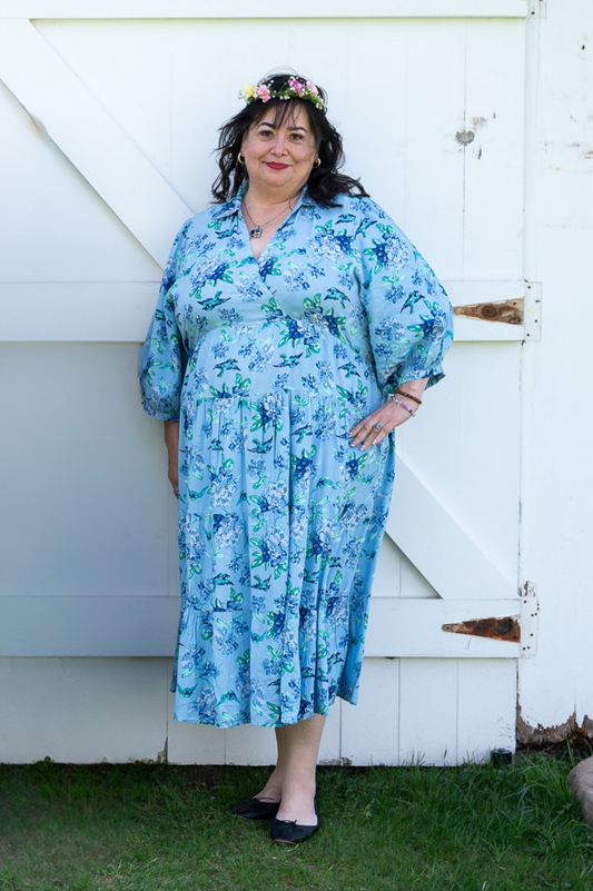Woman wearing a blue floral dress standing in front of a white wooden door.
