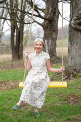 Keri in a floral dress sitting on a yellow swing in a park.