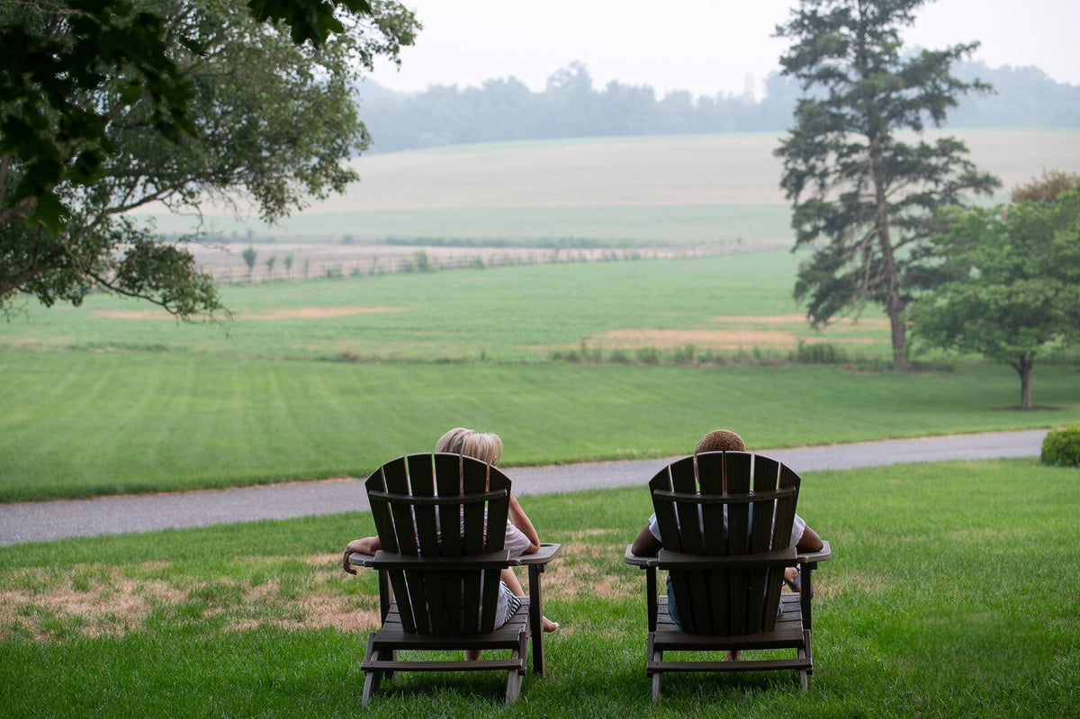 Two friends relaxing in Adirondack chairs overlooking a field